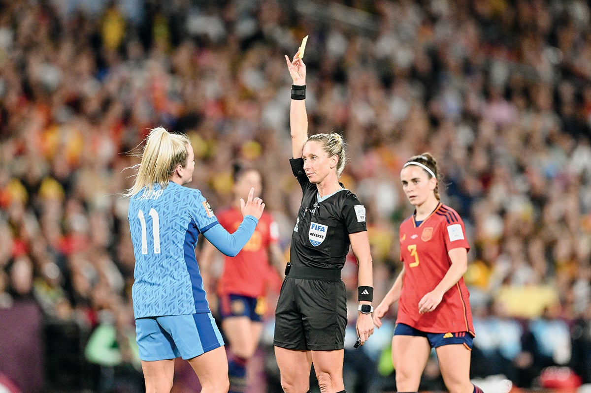 An action shot with two soccer players and a ref showing a yellow card.