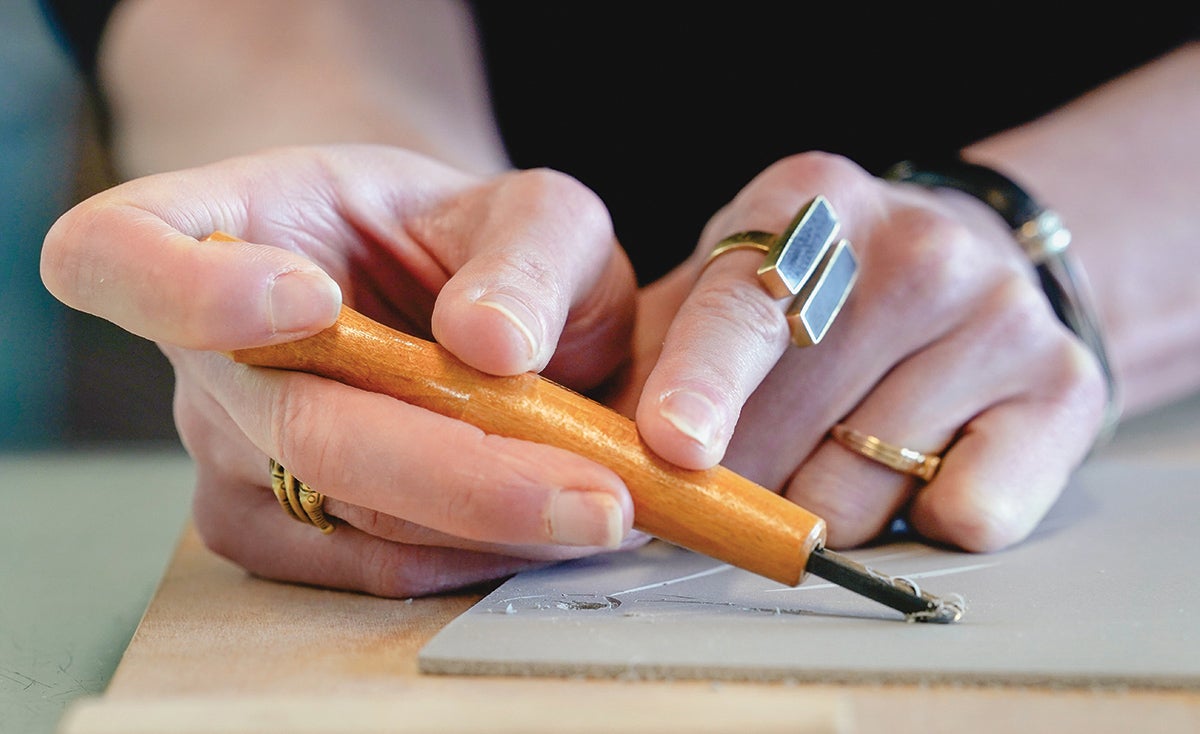 A close up of the two hands of a student demonstrating a printmaking technique.