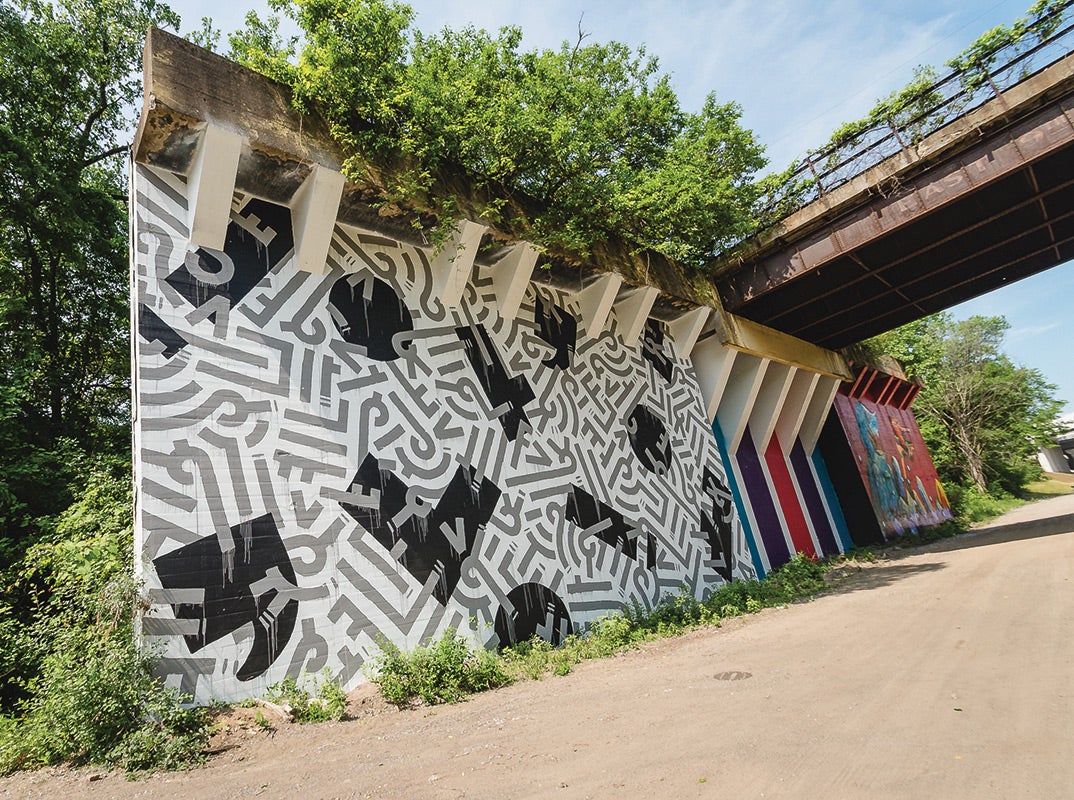 Image depicts mural made of black, white, and grey colors on a concrete wall under the Greater Cleveland Regional Transit Authority rapid-transit line