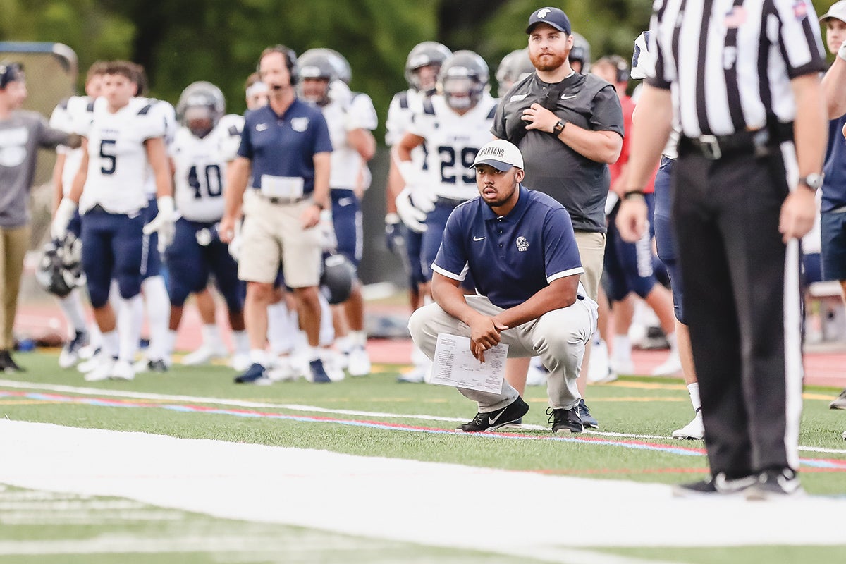Cameron Brown squatting on the football field while coaching a game