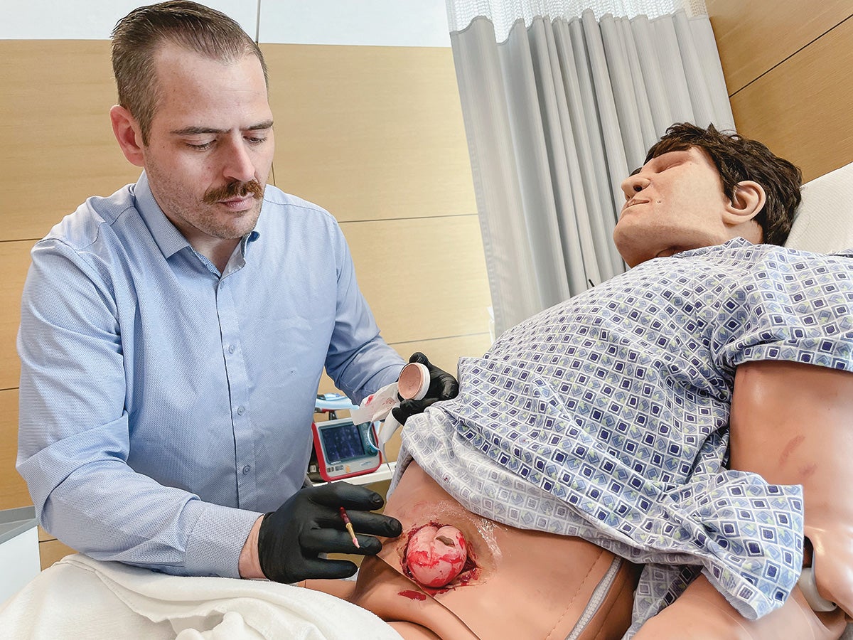 A person creating a simulation patient for nursing students by adding thick, syrup-like fake blood to mimic an abdominal hernia