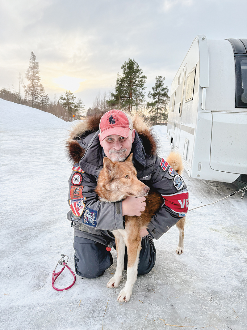 Lee Morgan kneeling and hugging a husky in Alaska