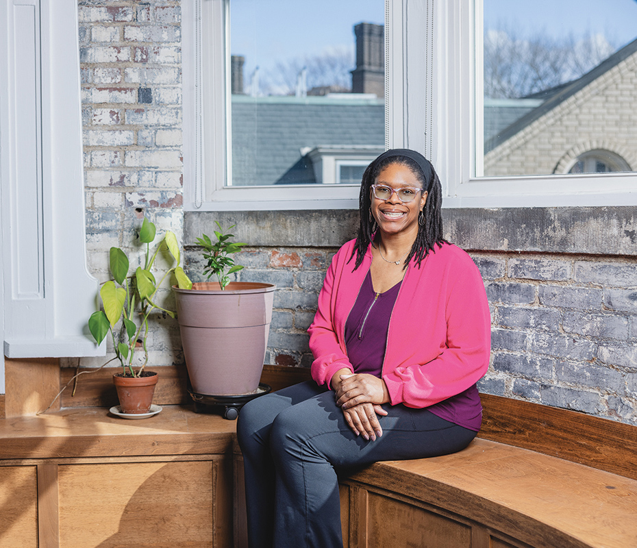 Image of Lakecia Wild sitting and smiling in front of a window with a plant next to her