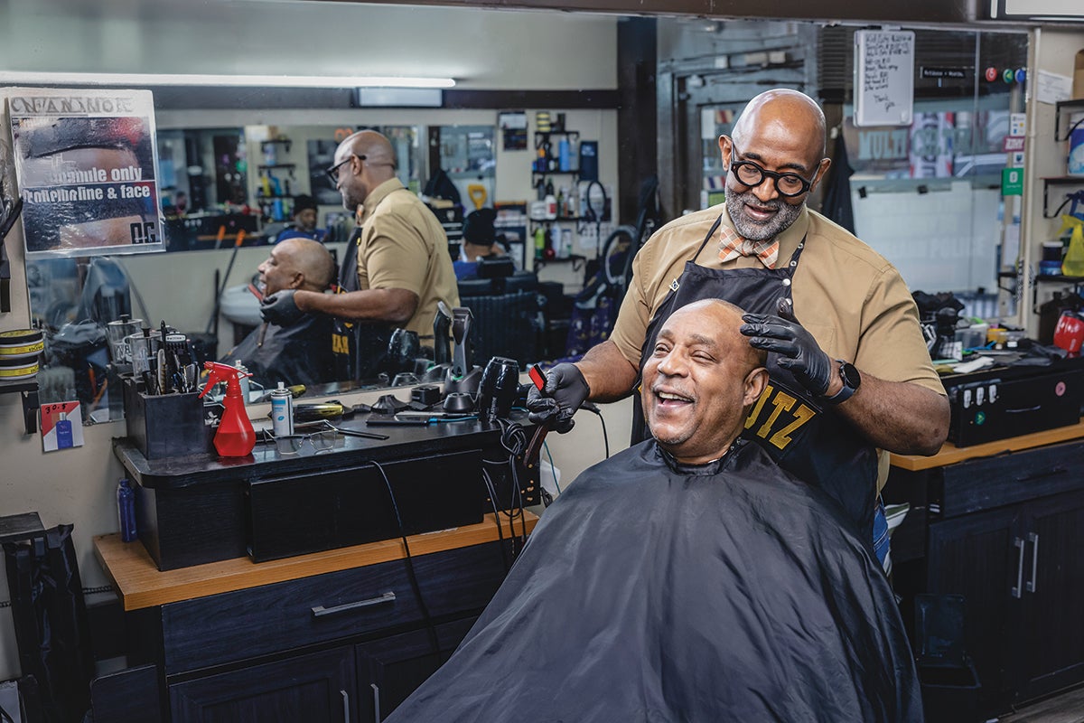A barber working on a client in a barbershop. Both look very happy.