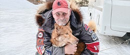 Lee Morgan kneeling and hugging a husky in Alaska
