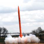 An orange rocket named "Once More" launches from a farm field.