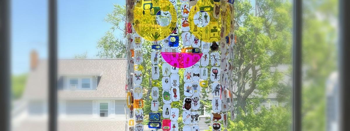 A mobile made of 200 shrinky-dink portraits with a plexiglass face.