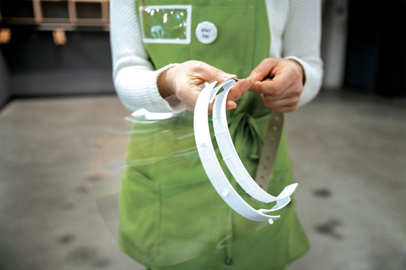A person wearing a green apron holds face shields