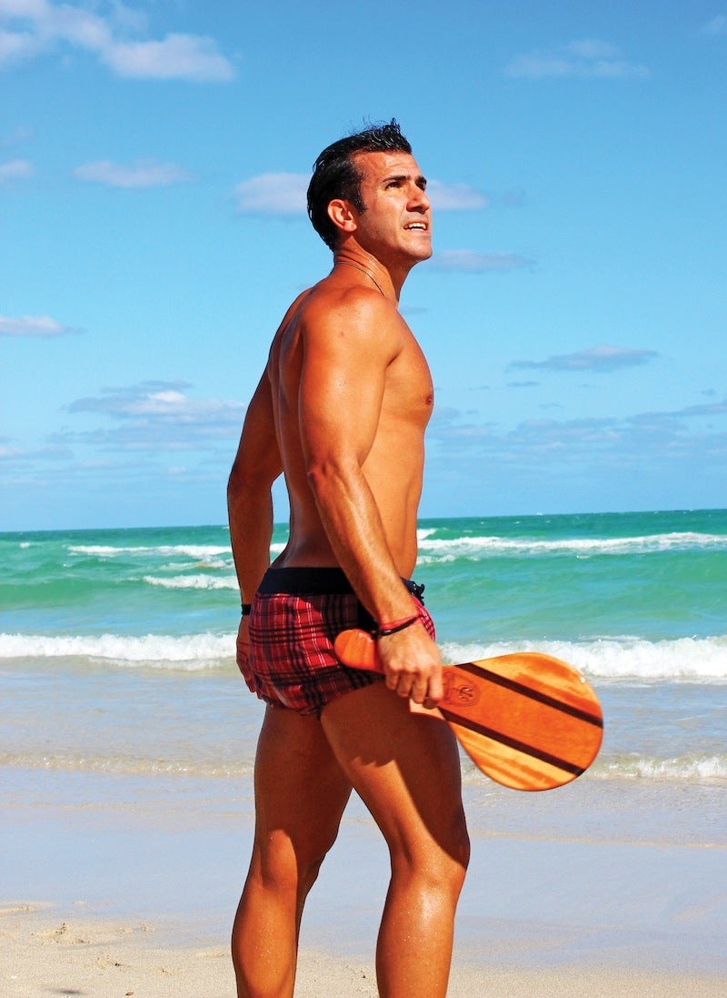 Man on the beach in a swimsuit holding a paddle 