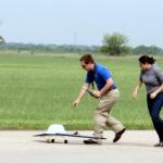 Two people running alongside a remote controlled airplane 