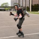 Ian Charnas skates on a parking lot with a jetpack on his back.