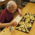 Frank Del Greco at a workbench, a replica street clock panel sits in front of him.
