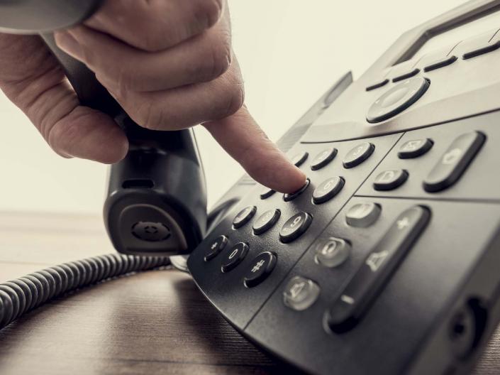 hand holding a phone receiver while dialing with the fingers