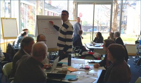 Staffer at a large white paper pad on an easel in front of seated staffers at a conference table
