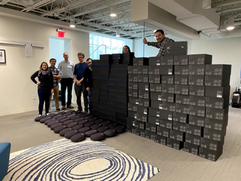 Seven people stand besides and behind boxes of HoloLens headsets before they are shipped to first year medical students.