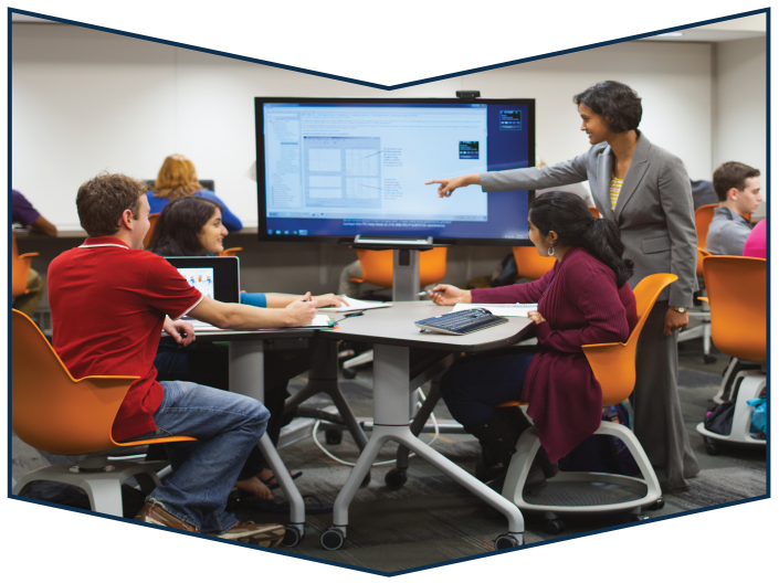 Engaged students gathered around monitor with instructor pointing at screen