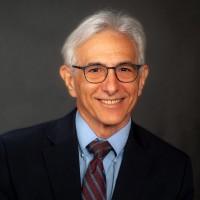 Headshot image of Doug Baumoel, a man wearing glasses, a dark suit and striped tie