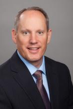 Headshot image of Scott Taylor, a man wearing a black suit jacket and red tie
