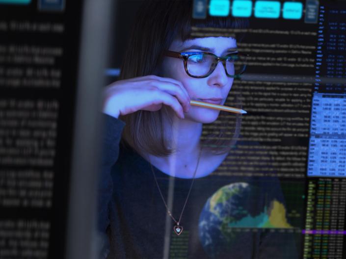 Stock image of a young woman studying a see through computer screen & contemplating.