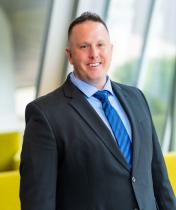 Headshot image of Chad Gepfrey, who is wearing a black suit and blue tie