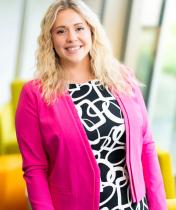 Headshot image of Victoria Schurr, who is wearing a pink blazer over a white-and-black dress