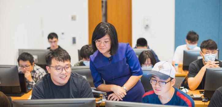 A professor helping two students at computers