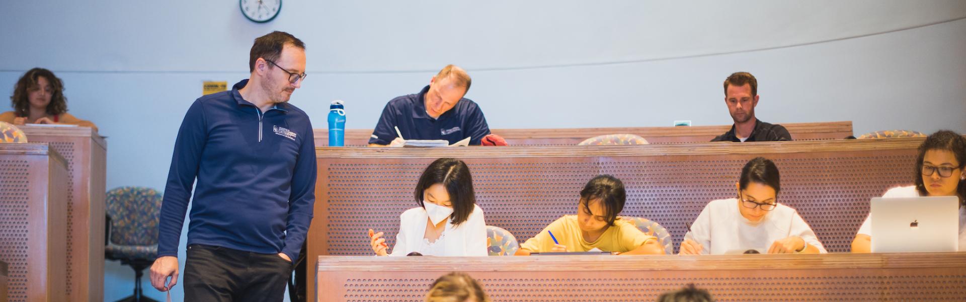 A faculty member watches students taking an exam in a lecture hall
