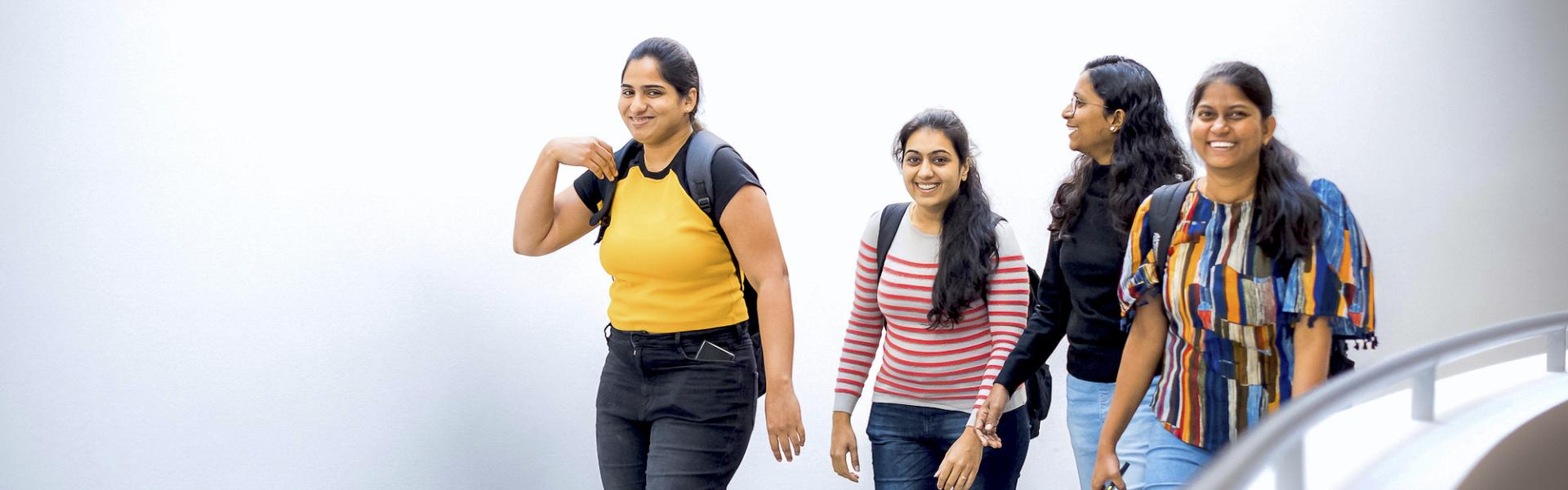 A group of femme students of color walk down hallway while smiling and laughing