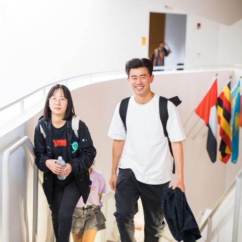 Smiling students ascend to the top of stairs into an open layout room