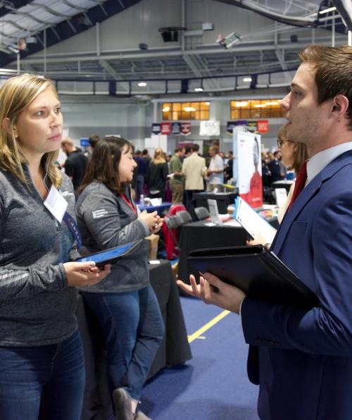 Representative from Avery Dennison speaks with a student wearing a suit at a career fair on campus