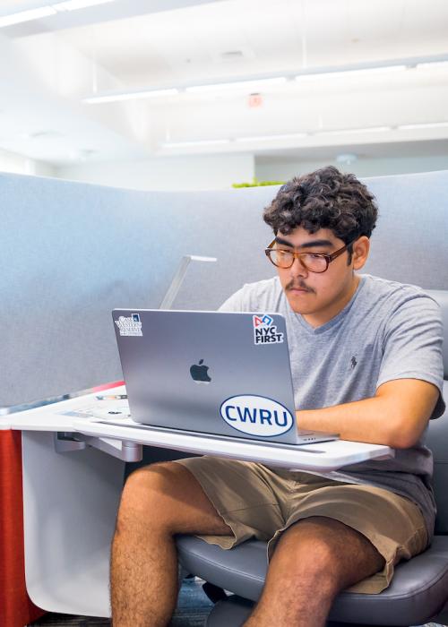 A student works on their laptop with a CWRU sticker in a cubicle