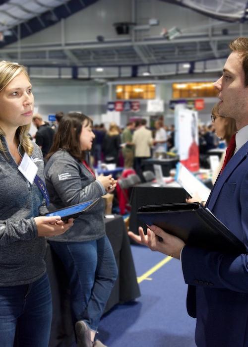 Representative from Avery Dennison speaks with a student wearing a suit at a career fair on campus