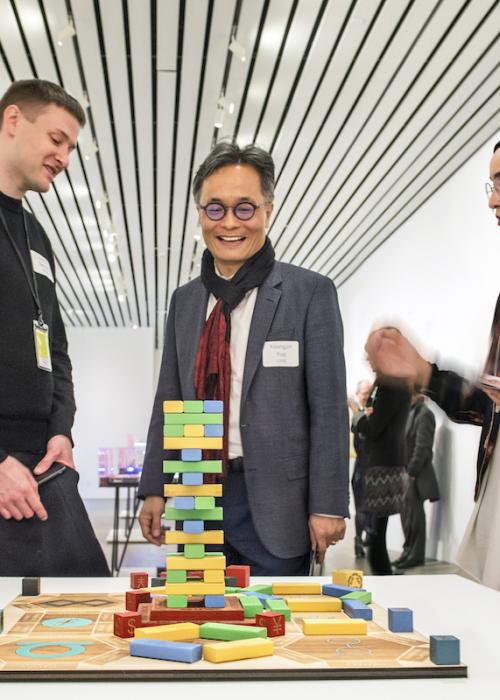 Faculty member Youngjin Yoo stands with two students by a table with a colorful Jenga game on it