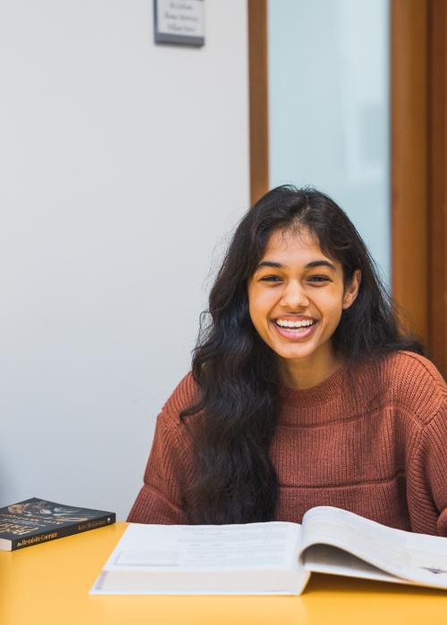 A femme student of color smiles with an open textbook