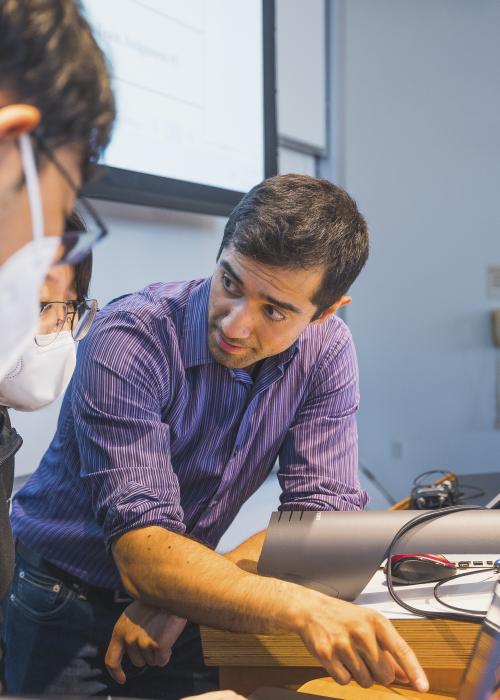 Instructor Jose Olavarria leans over a computer to help students
