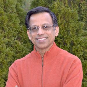 Portrait of Satish Nambisan smiling with evergreen trees in the background