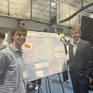 Andy Deneris and Jordan Perrott smile in front of their research poster at Intersections.
