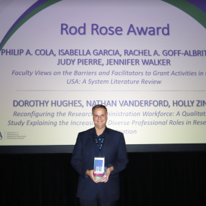 Phil Cola holds his Rod Rose Award on stage after being presented with it