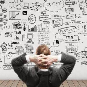 Man in gray business suit facing a giant white board of charts and graphs.