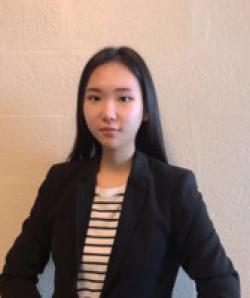 Yutong Wang smiles in a black suit jacket against a white background