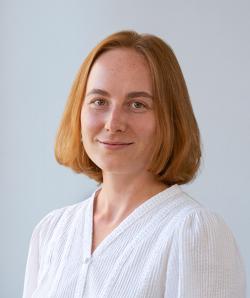 Varavara smiles in a white shirt against a grey background