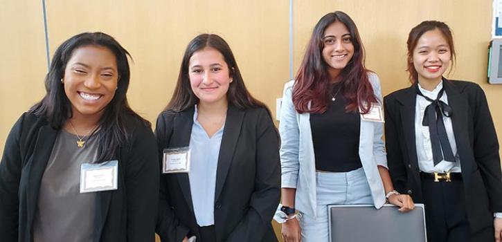 Four students smile while posing in business clothes. 