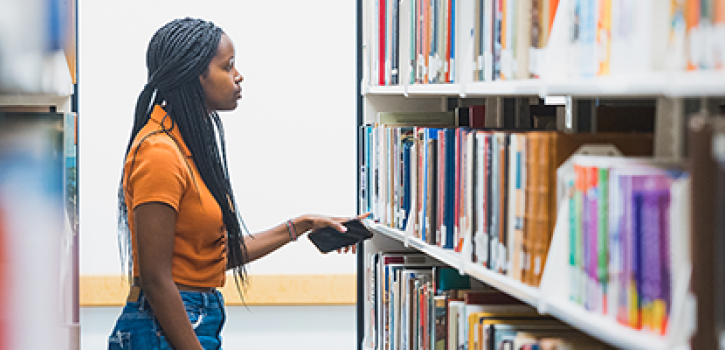 Case Western Reserve student stands facing shelves of books in Kelvin Smith Library