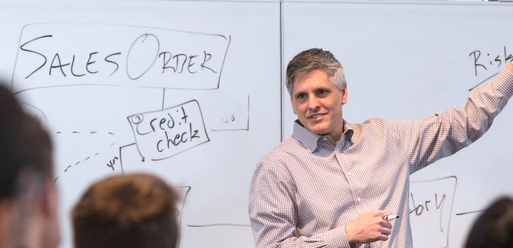 Faculty member Tony Bucaro stands before a class of students holding a dry-erase marker and gesturing