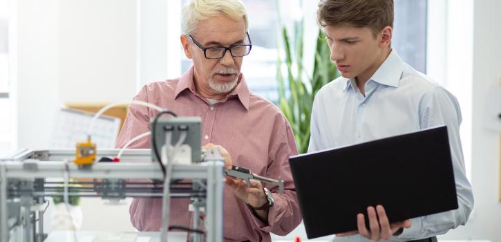 Stock photo featuring an older man on the left instructing a younger man in a hands-on laboratory setting
