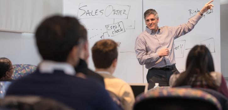 Faculty member teaches at the front of the classroom on a whiteboard.