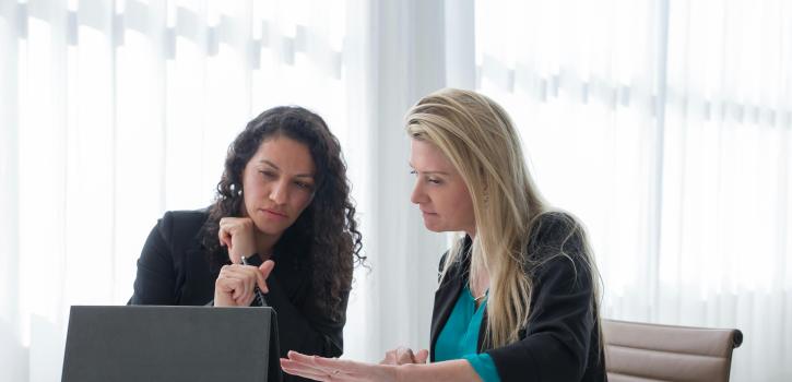 Two women sitting together viewing a computer while studying.