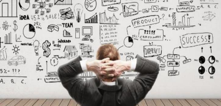 Man in gray business suit facing a giant white board of charts and graphs.