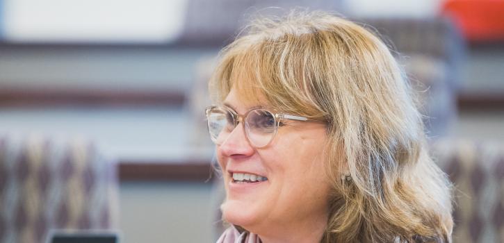 An older student wearing a scarf sits in class and smiles towards the lecturer.