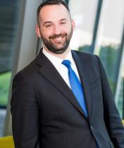 Headshot image of Kevin Lenahan, who is wearing a black suit jacket and blue tie